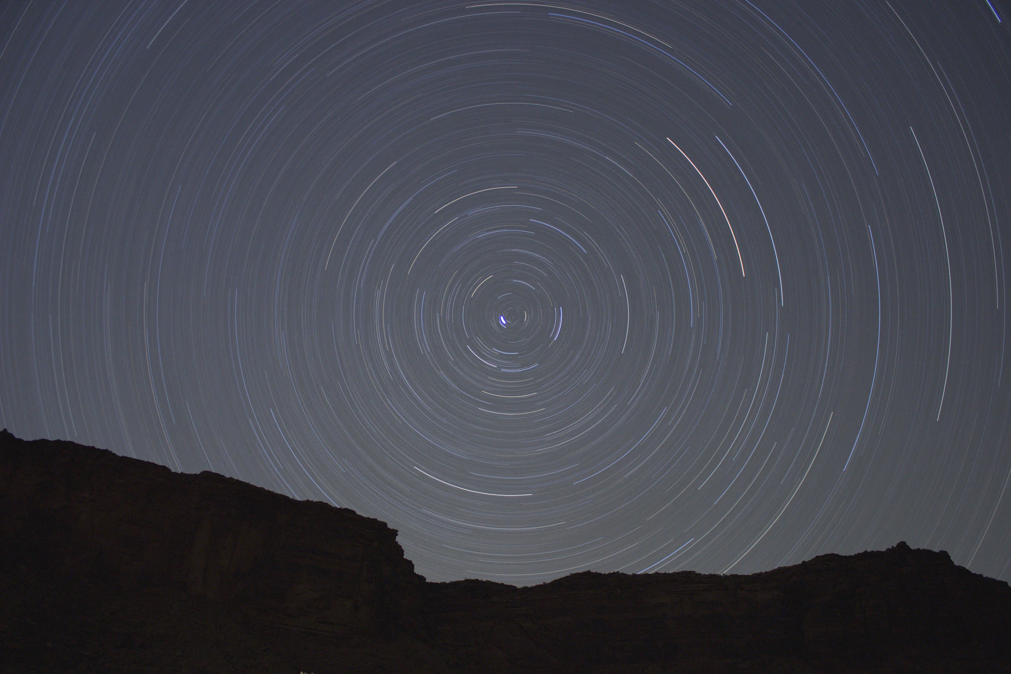 Star trails circling the celestial pole above a dark canyon ridge, the sky turning over one night
